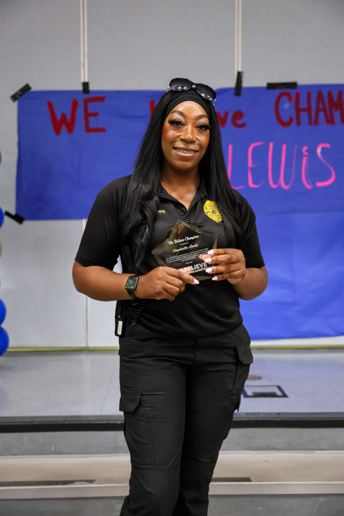 We Believe Champion holding a commemorative plaque in front of a We Believe Champion banner