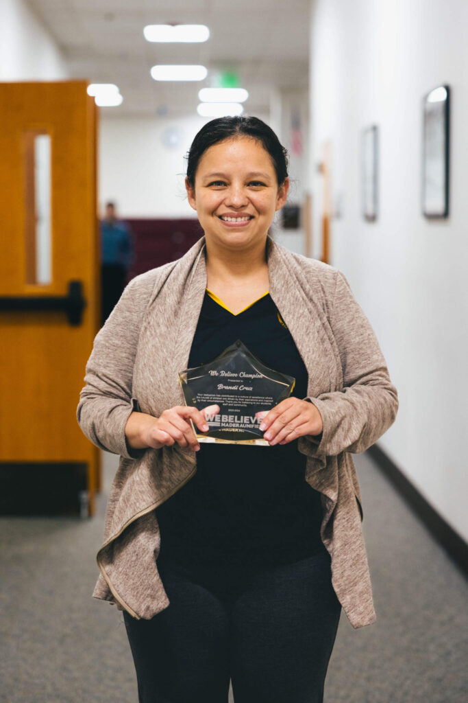 We Believe Champion holding a commemorative plaque in a school hallway