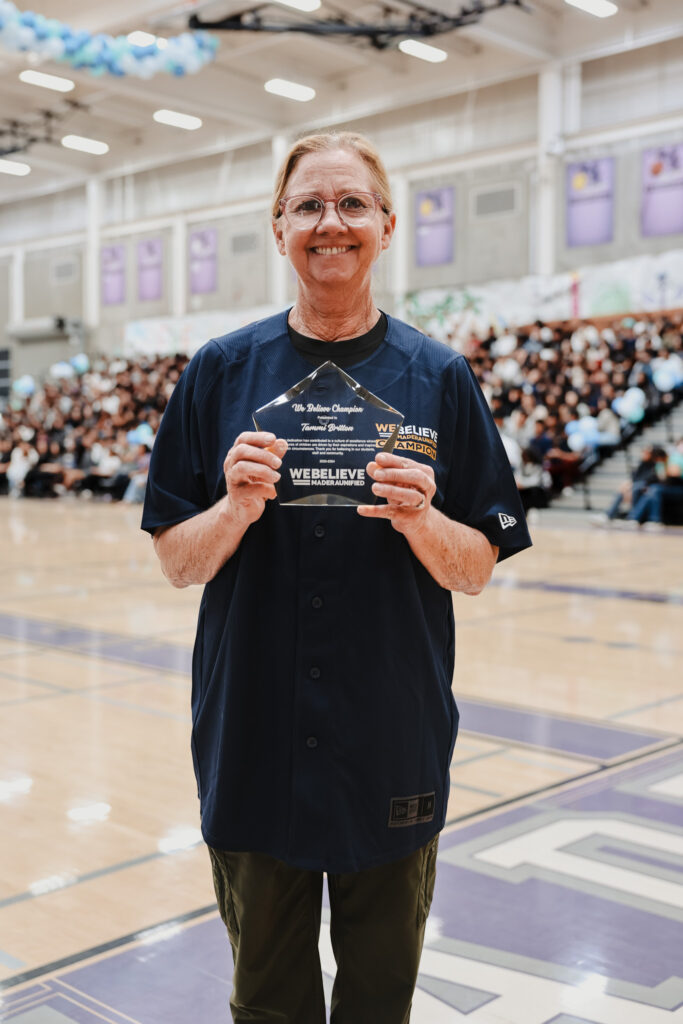 We Believe Champion holding a commemorative plaque in a school gym
