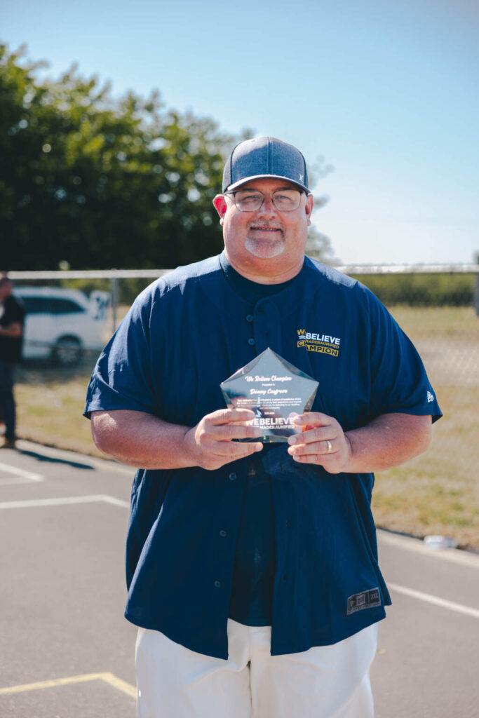 We Believe Champion holding a commemorative plaque outdoors